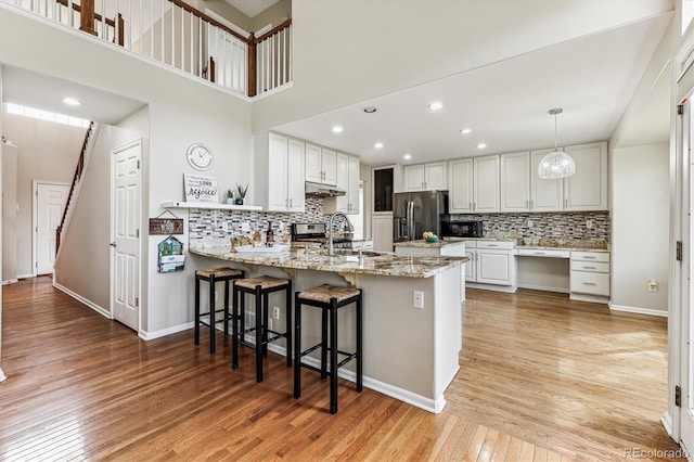 kitchen with light hardwood / wood-style flooring, decorative light fixtures, kitchen peninsula, appliances with stainless steel finishes, and white cabinets