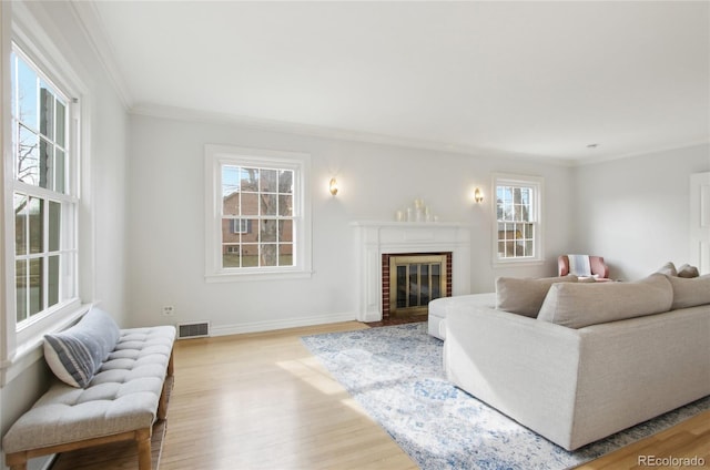 living room with crown molding, a healthy amount of sunlight, a fireplace, and light hardwood / wood-style flooring