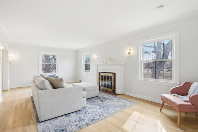 living room with a brick fireplace, crown molding, and light wood-type flooring