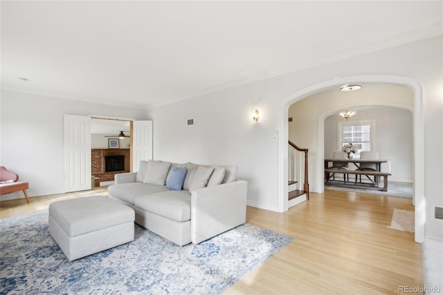 living room featuring hardwood / wood-style flooring, ornamental molding, a brick fireplace, and a notable chandelier