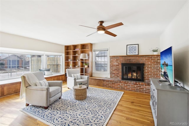 living room featuring a brick fireplace, light hardwood / wood-style flooring, and ceiling fan