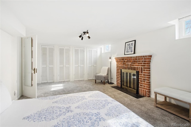 carpeted bedroom featuring a brick fireplace and two closets