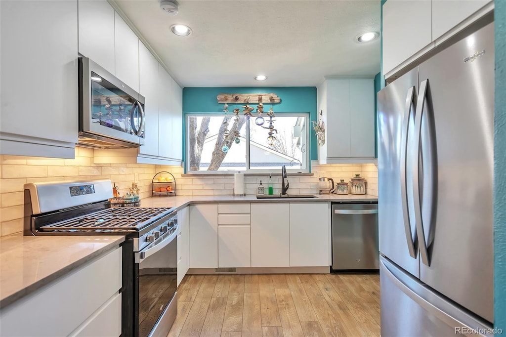 kitchen featuring backsplash, stainless steel appliances, sink, white cabinets, and light hardwood / wood-style floors