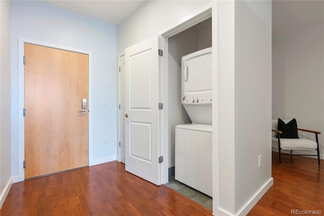 clothes washing area featuring baseboards, stacked washer / drying machine, wood finished floors, and laundry area