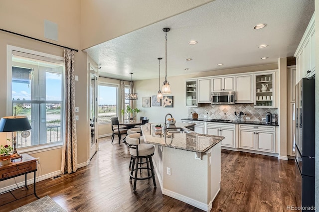 3181 Firenze Pl, Highlands Ranch, CO 80126 - kitchen with appliances with stainless steel finishes, a sink, decorative backsplash, glass insert cabinets, and a breakfast bar area