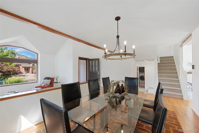 dining room featuring washer / dryer, vaulted ceiling, an inviting chandelier, and light hardwood / wood-style flooring