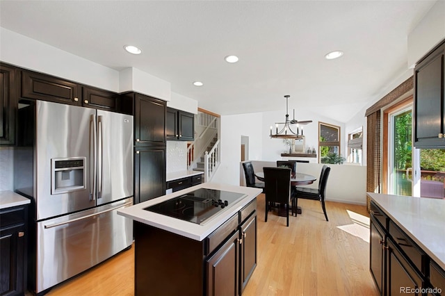 kitchen featuring light hardwood / wood-style floors, vaulted ceiling, a kitchen island, black electric cooktop, and stainless steel fridge