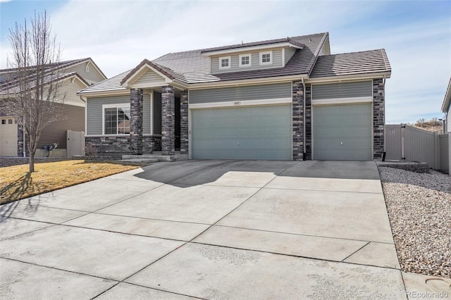 view of front of home with driveway, stone siding, a tiled roof, an attached garage, and fence