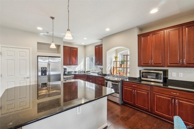 kitchen featuring dark stone countertops, stainless steel appliances, dark wood finished floors, and decorative light fixtures