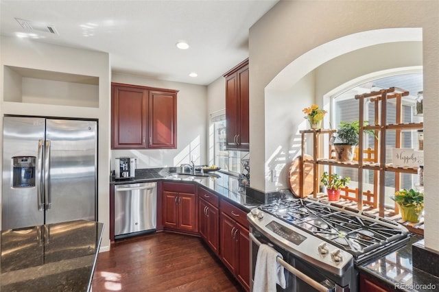 kitchen with dark wood finished floors, visible vents, appliances with stainless steel finishes, a sink, and dark brown cabinets