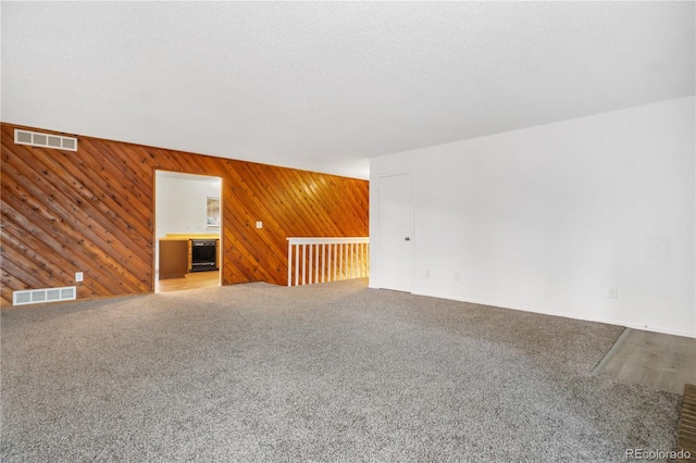 unfurnished room with carpet flooring, a textured ceiling, and wood walls