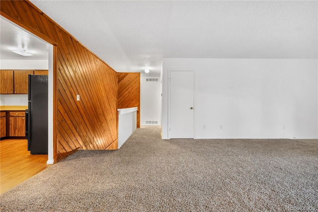 bonus room with wood walls, light colored carpet, and a textured ceiling