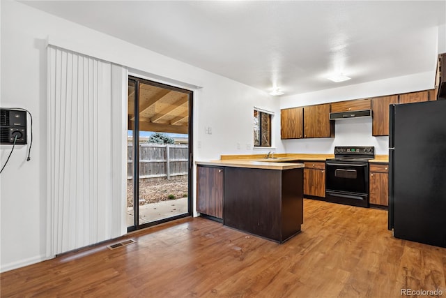 kitchen with black appliances, sink, light hardwood / wood-style flooring, kitchen peninsula, and a wall unit AC