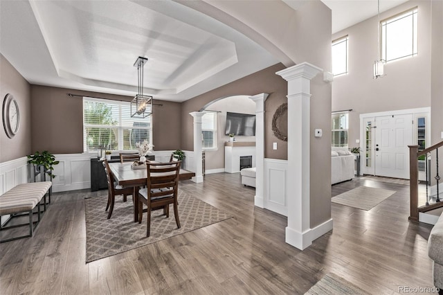 dining space featuring ornate columns, a raised ceiling, arched walkways, wainscoting, and a decorative wall