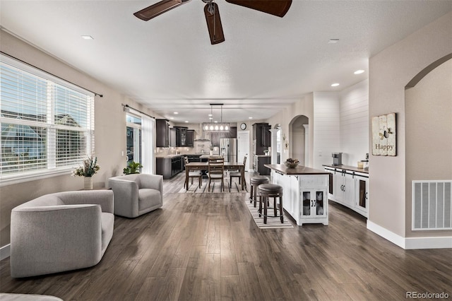 living room featuring arched walkways, ceiling fan, dark wood-style floors, baseboards, and recessed lighting