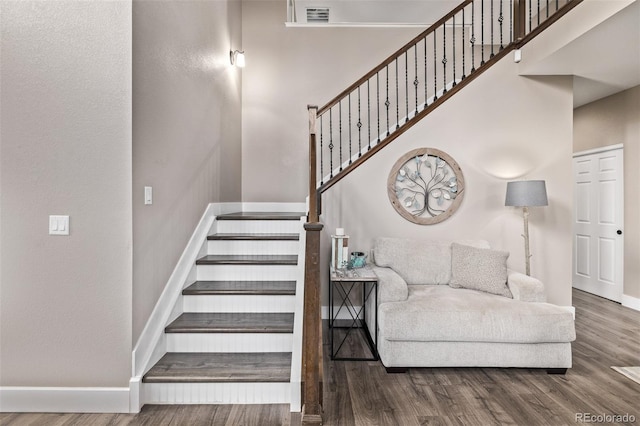 stairway featuring baseboards, wood finished floors, and a towering ceiling