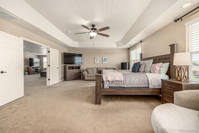 bedroom with a tray ceiling, light carpet, multiple windows, and a ceiling fan