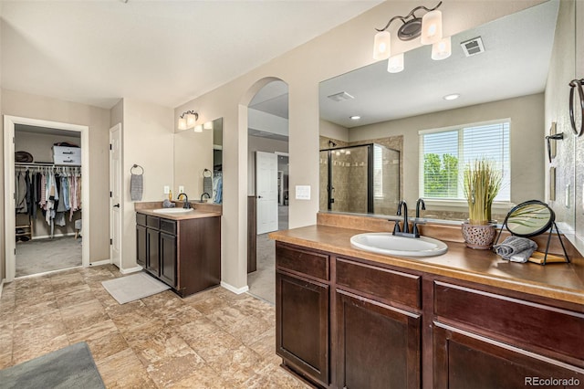 full bath featuring a shower stall, two vanities, a spacious closet, and baseboards