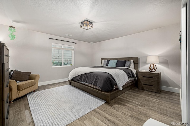 bedroom featuring baseboards, a textured ceiling, and wood finished floors