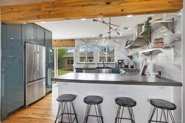 882 E Briarwood Cir, Centennial, CO 80122 - kitchen with wall chimney range hood, dark countertops, stainless steel refrigerator, a sink, and a peninsula