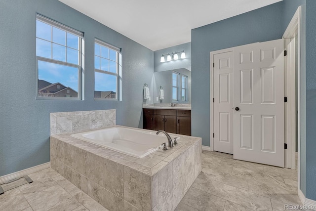 bathroom with vanity, a bath, a textured wall, and baseboards