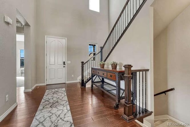 entryway featuring a towering ceiling, stairs, baseboards, and wood finished floors