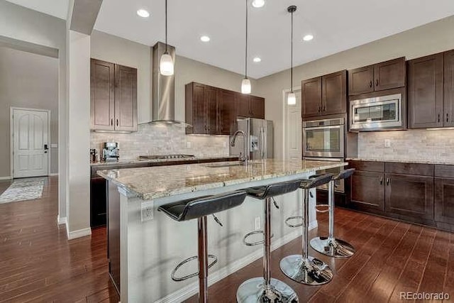 kitchen featuring dark brown cabinets, dark wood finished floors, appliances with stainless steel finishes, wall chimney exhaust hood, and a sink