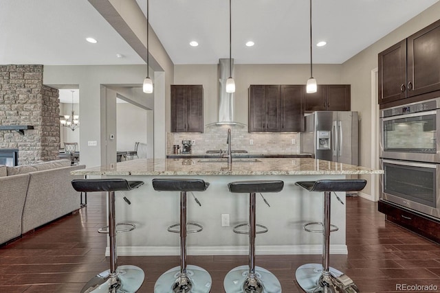 kitchen with dark brown cabinets, dark wood finished floors, open floor plan, a breakfast bar, and stainless steel appliances