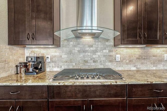 kitchen featuring wall chimney range hood, dark brown cabinets, light stone countertops, and stainless steel gas cooktop