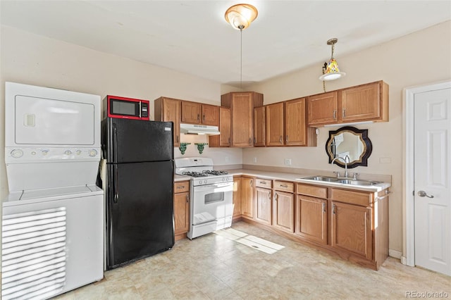 kitchen featuring black refrigerator, gas range gas stove, sink, pendant lighting, and stacked washer / dryer