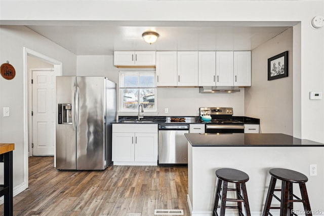 kitchen featuring dark countertops, stainless steel appliances, wood finished floors, white cabinetry, and a sink