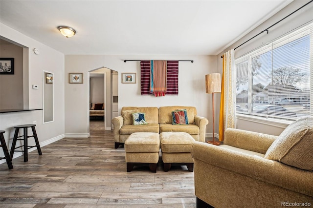 living area featuring arched walkways, baseboards, and wood finished floors