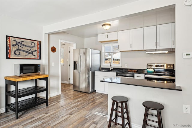 kitchen featuring dark countertops, under cabinet range hood, a kitchen bar, appliances with stainless steel finishes, and a sink