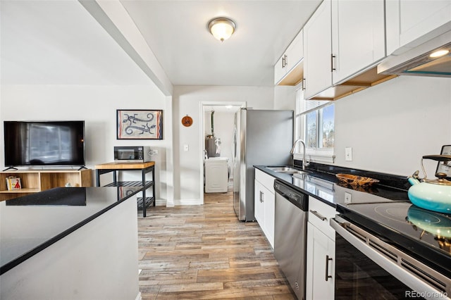 kitchen featuring dark countertops, stainless steel appliances, light wood-style floors, white cabinetry, and a sink