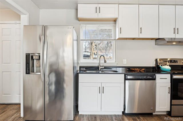 kitchen with a sink, dark countertops, white cabinetry, stainless steel appliances, and wall chimney exhaust hood