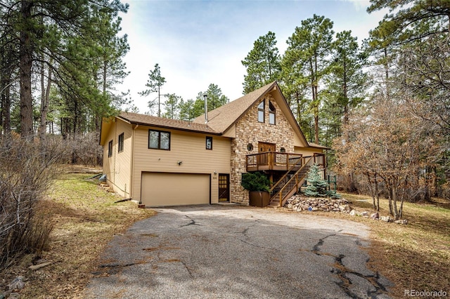 rustic home featuring a garage, stone siding, stairs, driveway, and a deck