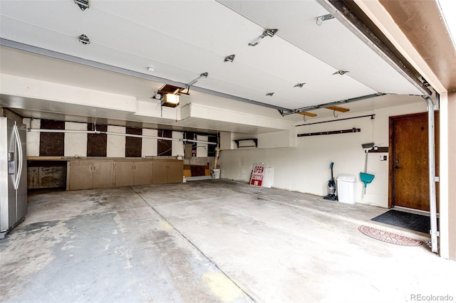 garage with stainless steel refrigerator with ice dispenser and a garage door opener