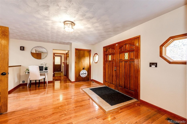 entrance foyer featuring light wood-style flooring, baseboards, and a textured ceiling