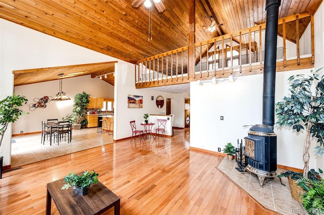 living area featuring wood-type flooring, a wood stove, wooden ceiling, and baseboards