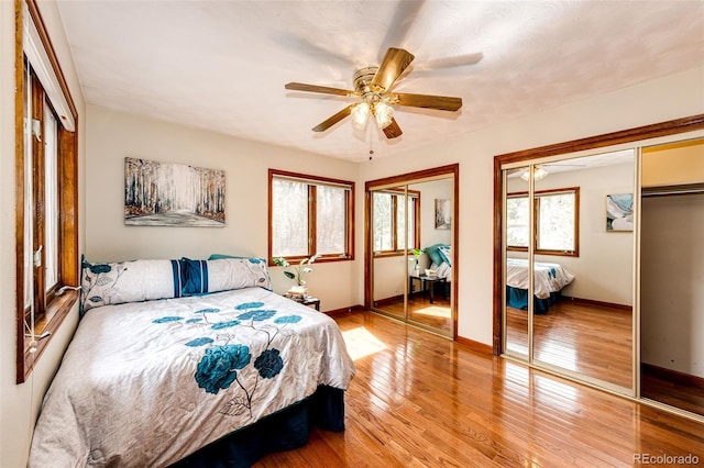 bedroom with baseboards, light wood-type flooring, two closets, and ceiling fan
