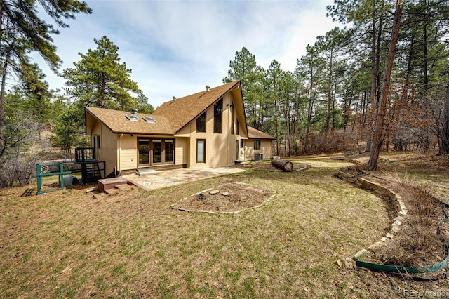 rear view of property with roof with shingles, a patio area, and a lawn