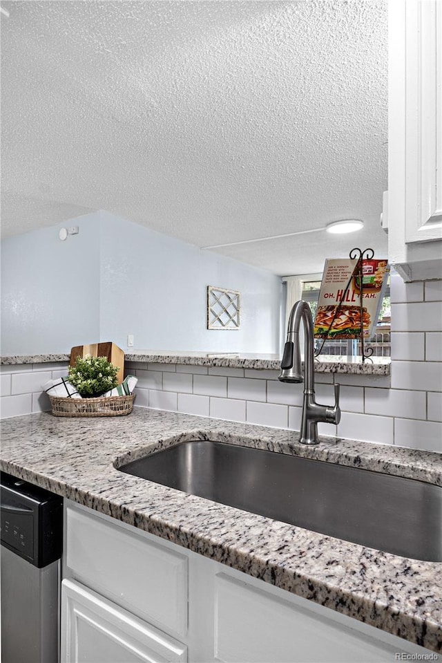 2281 Vaughn Unit 104A, Aurora, CO 80014 - kitchen view of a sink, a textured ceiling, tasteful backsplash, white cabinetry, and stainless steel dishwasher