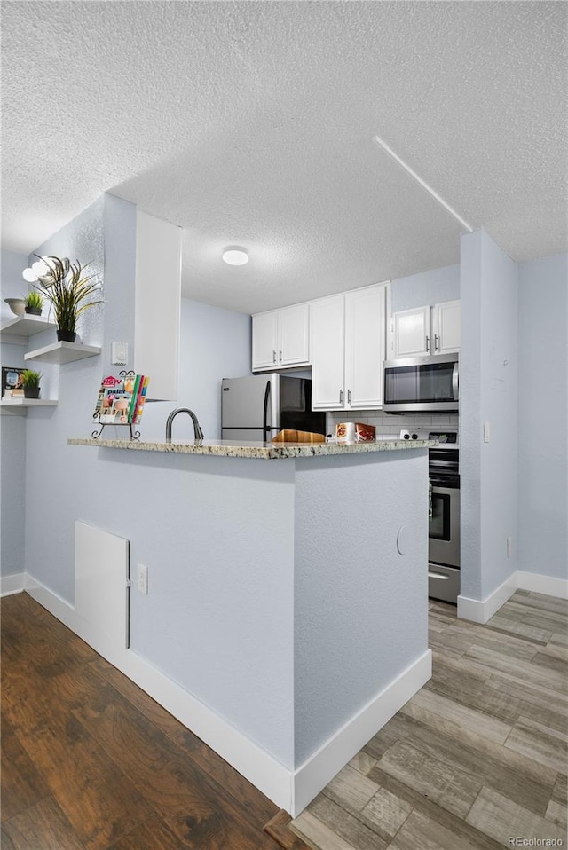 2281 Vaughn Unit 104A, Aurora, CO 80014 - kitchen featuring appliances with stainless steel finishes, a textured ceiling, white cabinetry, wood finished floors, and baseboards