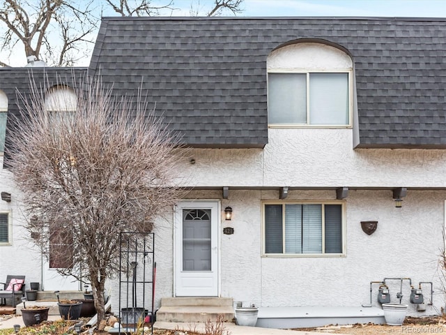 view of front of property featuring a shingled roof, entry steps, stucco siding, and mansard roof