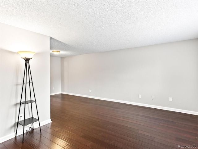 spare room with baseboards, dark wood finished floors, and a textured ceiling