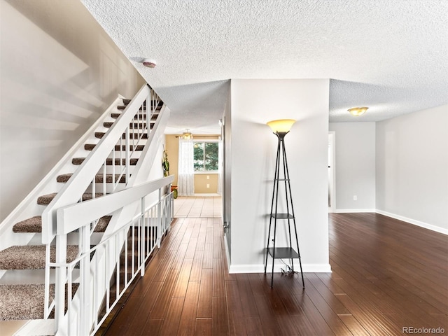 hallway with stairway, dark wood-style flooring, a textured ceiling, and baseboards