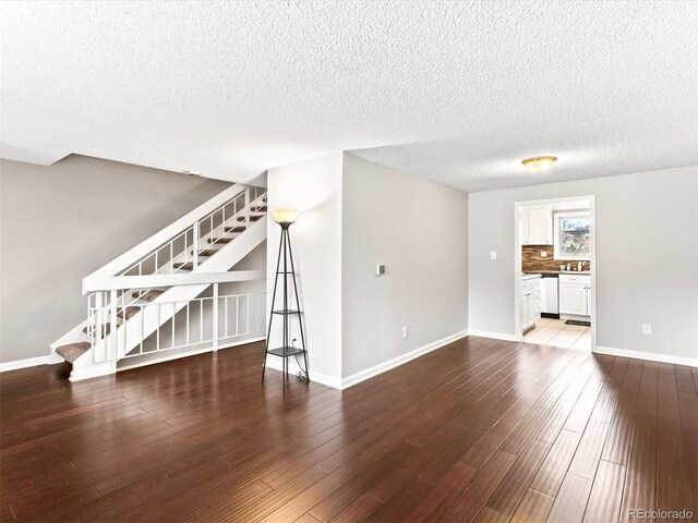 unfurnished living room featuring baseboards, a textured ceiling, stairway, and wood finished floors