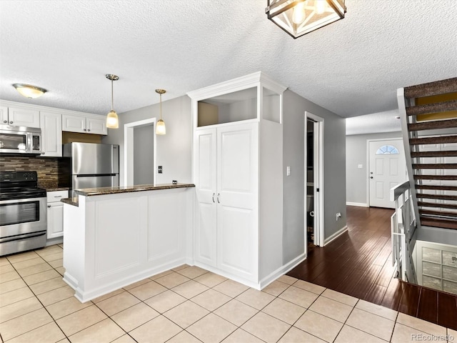 kitchen with light tile patterned floors, backsplash, appliances with stainless steel finishes, white cabinets, and a peninsula