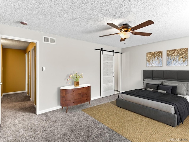 carpeted bedroom featuring visible vents, a barn door, ceiling fan, a textured ceiling, and baseboards