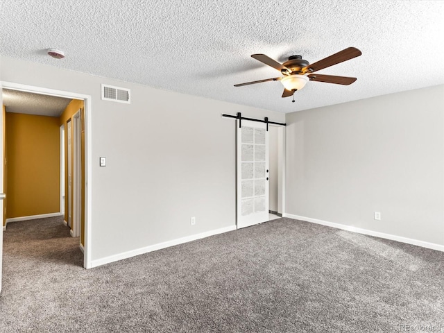 carpeted spare room with visible vents, a barn door, a ceiling fan, a textured ceiling, and baseboards